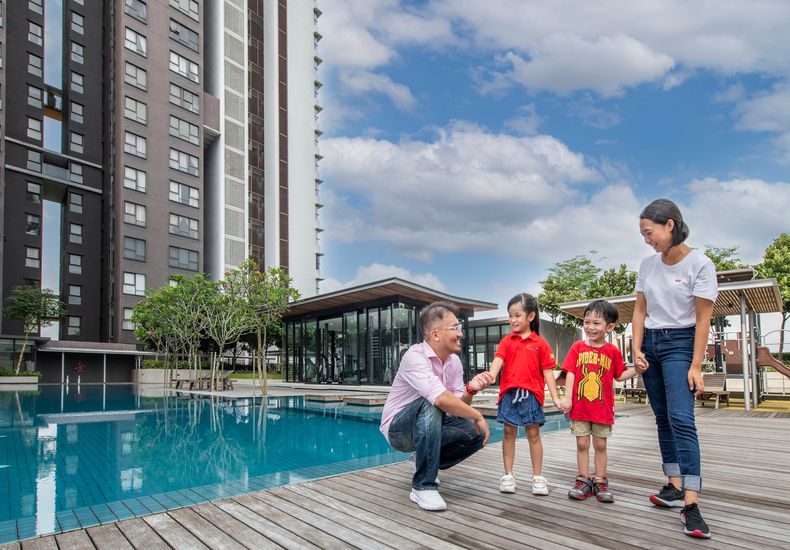 A laughing family standing on a poolside deck at the base of a modern apartment tower at Senibong Cove.